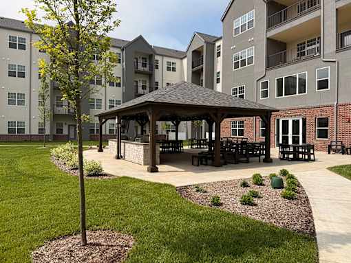 A gazebo sits in the middle of a grassy area in front of apartment buildings.