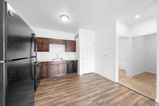 A black refrigerator is on the left in a kitchen with wooden floors. at Union at the Loop, Lawrence, KS