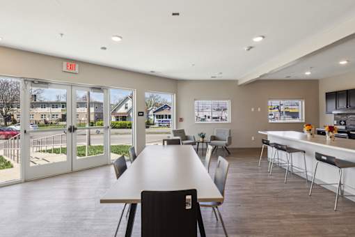 A large room with a long table and chairs, a kitchen area, and a view of the outside through the glass doors at Union at 16th, Indianapolis, IN