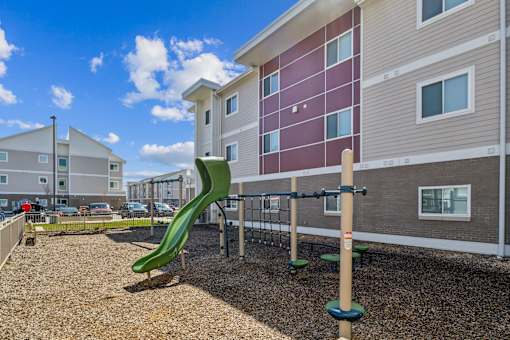 A playground with a green slide in front of a building at Union at 16th, Indianapolis, IN