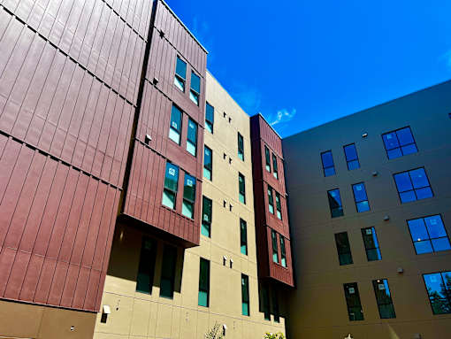 A tall building with a red and beige facade stands under a blue sky.