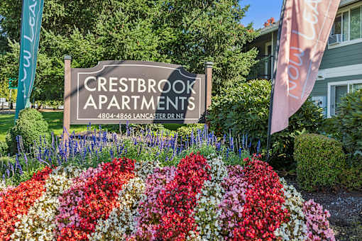 A sign for Crestbrook Apartments is displayed in front of a flower bed.