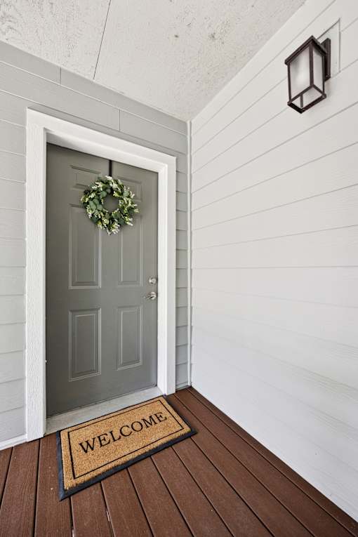 A grey door with a wreath and a welcome mat on a wooden floor.