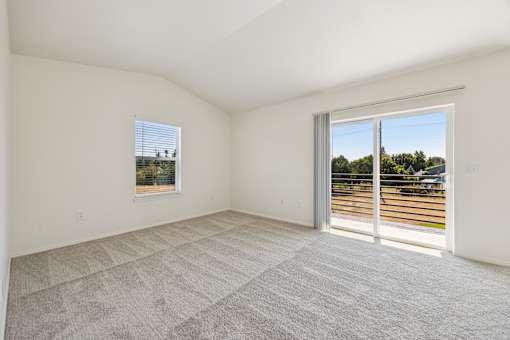 A room with a carpeted floor and a sliding glass door leading to a parking lot.