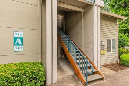 A staircase with a blue railing leads to a doorway with a sign that reads 212 A 112.