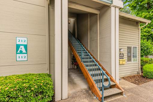 A staircase with a blue railing leads to a doorway with a sign that reads 212 A 112.