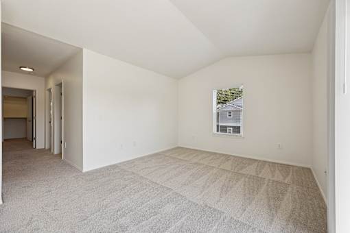 A sparsely furnished room with a carpeted floor and a window showing a house outside.