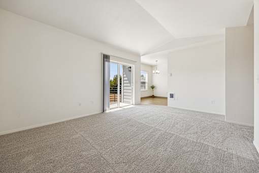 A large, empty room with a carpeted floor and a sliding glass door leading to a balcony.