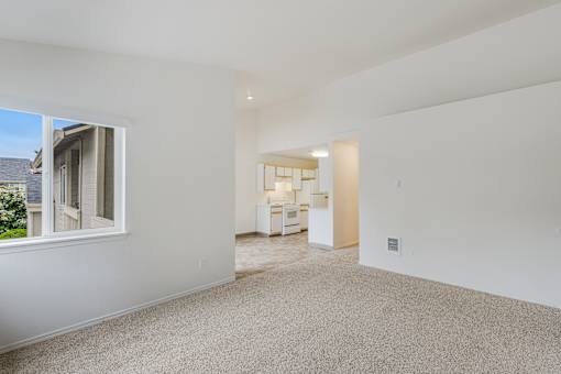 A large empty room with a window and a door leading to another room.