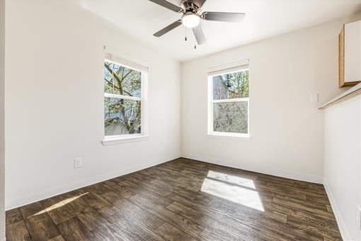 A room with a ceiling fan and two windows.