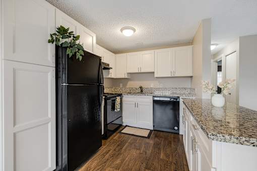 A black fridge in a kitchen with white cabinets.