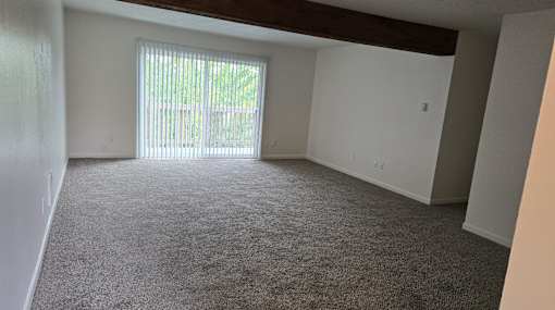 A room with a carpeted floor and a window with blinds.