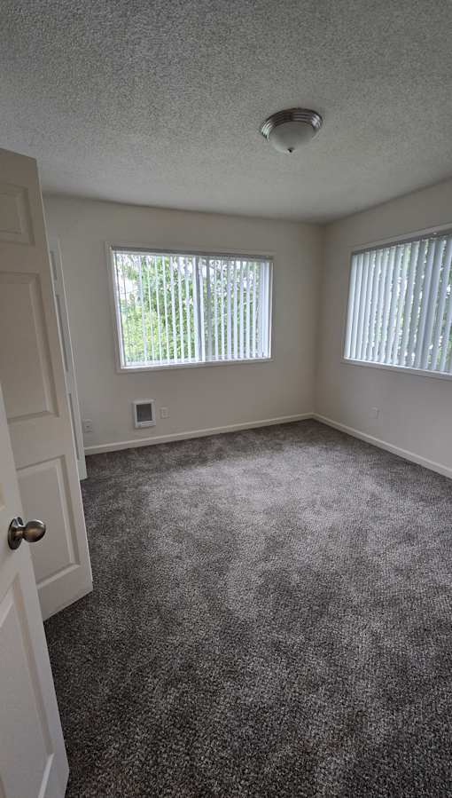 A room with a carpeted floor and a window with blinds.