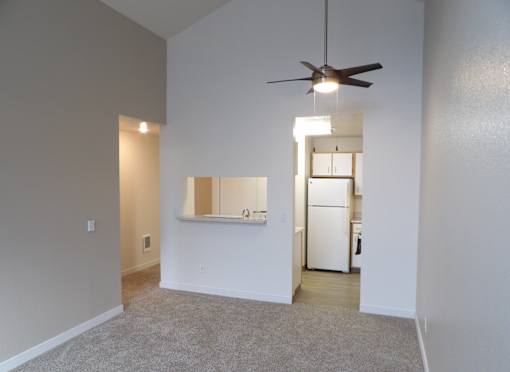 A room with a ceiling fan and a small kitchen area in the background.