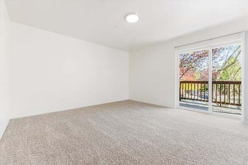 A room with a carpeted floor and a window with a view of a fence and trees.