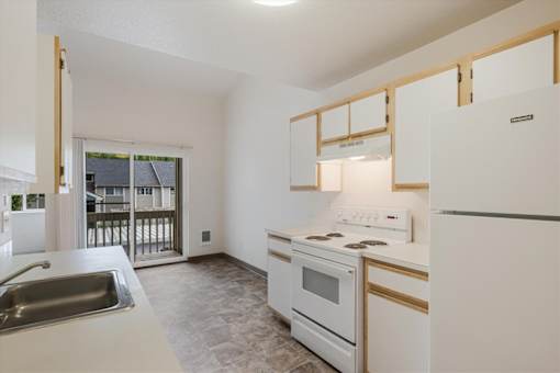 A kitchen with white appliances and a window overlooking a balcony.