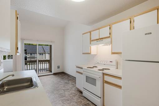 A kitchen with white appliances and a window overlooking a balcony.
