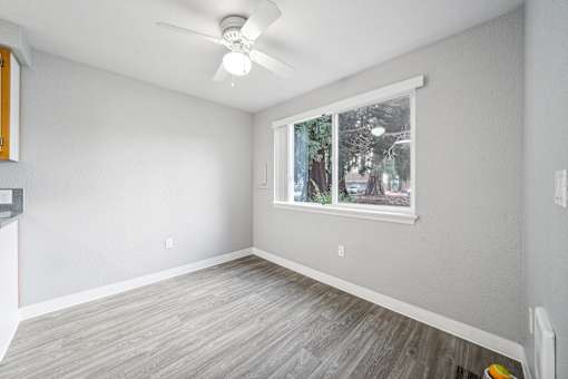 A room with a ceiling fan and a window showing trees outside.