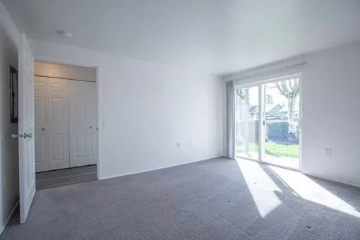 A large empty room with a carpeted floor and a sliding glass door leading outside.
