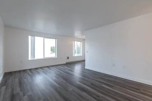 A room with wooden flooring and two windows.