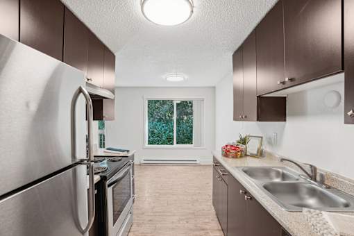A kitchen with a stainless steel refrigerator and a window with greenery outside.