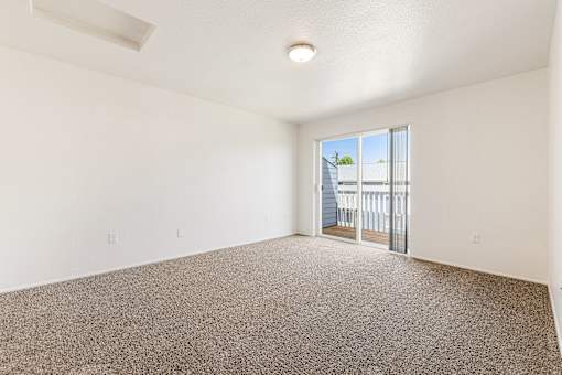 A room with a carpeted floor and a sliding glass door leading to a balcony.