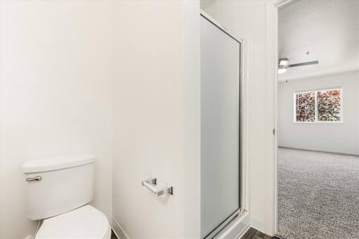 A white toilet in a small bathroom with a glass door leading to a hallway.