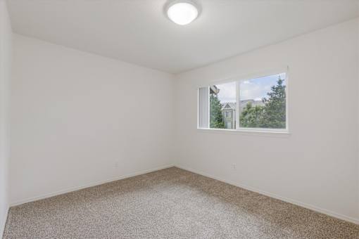 A room with a carpeted floor and a window showing a view of a house and trees.
