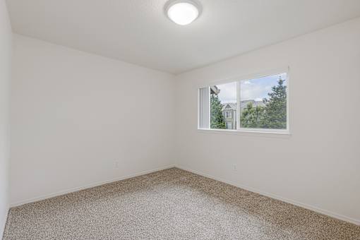 A room with a carpeted floor and a window showing a view of a house and trees.