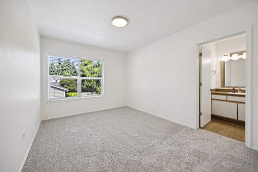 A room with a carpeted floor and a window showing a view of trees and a house.