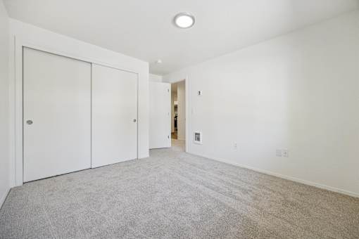 A room with white walls and a carpeted floor with a white door on the left and a white closet door on the right.