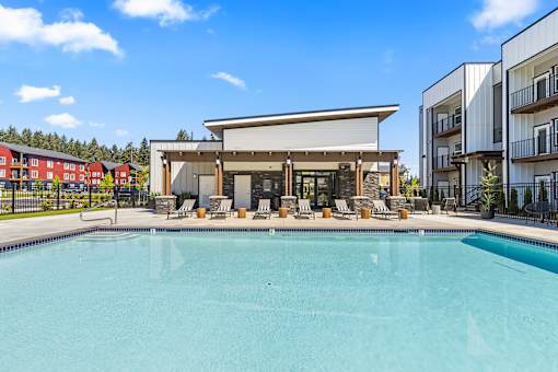 A large swimming pool in front of a building with a sun lounger.