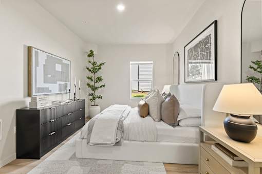 A modern bedroom with a large bed, a black dresser, and a grey rug.