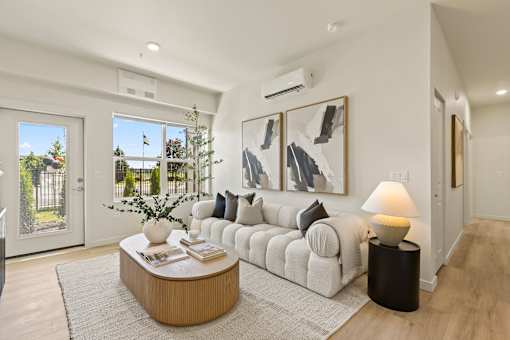A modern living room with a white sofa, a wooden coffee table, and a large window with a view of the garden.
