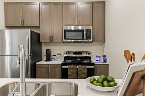 A kitchen with a refrigerator, microwave, oven, and a bowl of green fruit on the counter.
