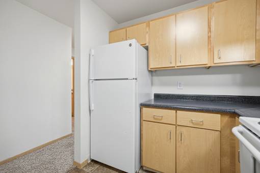 A white refrigerator is in a kitchen with wooden cabinets.
