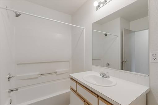 A white bathroom with a sink, mirror, and bathtub.