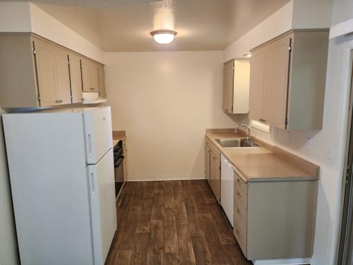 an empty kitchen with white appliances and wood flooring