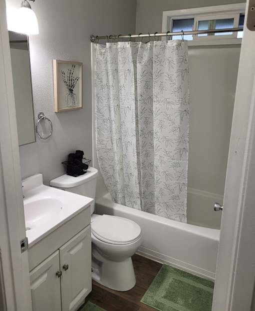 A white bathroom with a green rug on the floor.