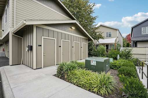 A building with a grey roof and a green trash bin in front of it.