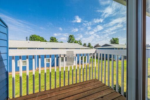 A view from a porch looking out at a blue building and green lawn.