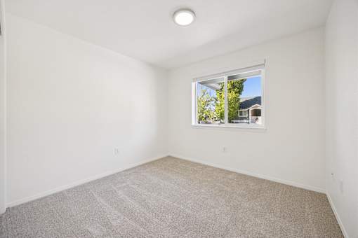 A room with a carpeted floor and a window showing a house and trees outside.