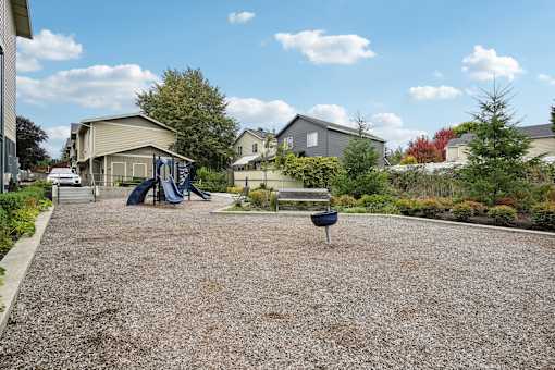A playground with a slide, swings, and a bench in the middle of a gravel area.