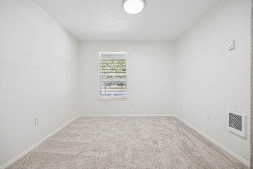 A room with a carpeted floor and a window with blinds.