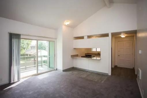 A spacious room with a kitchen area and a sliding glass door leading to a balcony.