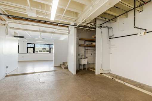 A large, empty room with a kitchenette in the back.