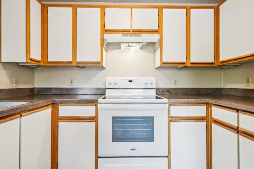 A white stove is in a kitchen with wooden cabinets.