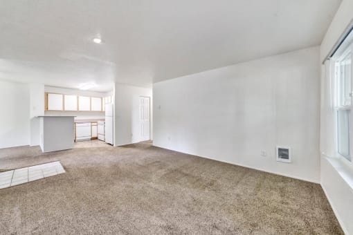 the living room and kitchen of an empty house with carpeting and white walls