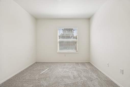 A room with a carpeted floor and a window with blinds.