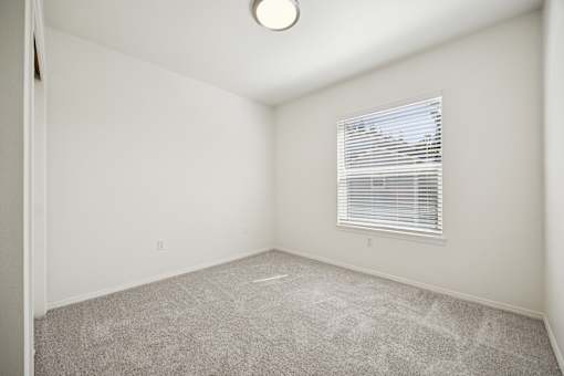A room with a carpeted floor and a window with blinds.